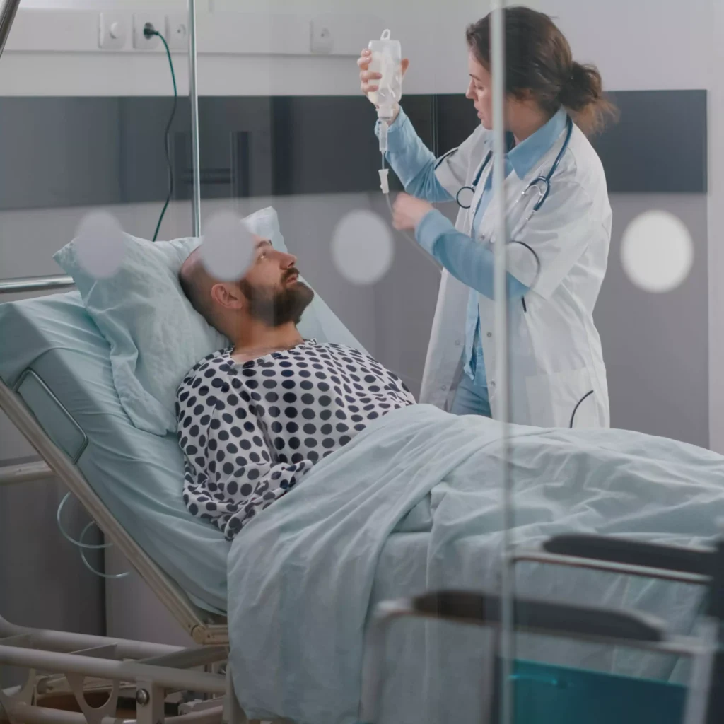 A patient receiving critical care at home in Ranchi, with a nurse attending to him in a hospital bed