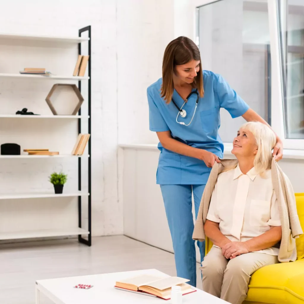 A caring nurse assisting an elderly woman on a couch, providing comfort and support. नर्स कैसे बने ? Ranchi patient care services, nurse at home